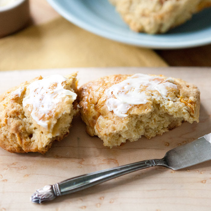 Close-up of split Einkorn scone topped with butter, showing flaky crumb and apricot pieces on wooden board with knife