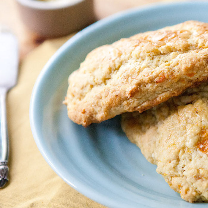 Close-up side view of two Einkorn scones with crystallized ginger and apricot pieces showing flaky golden-brown crust on a blue plate