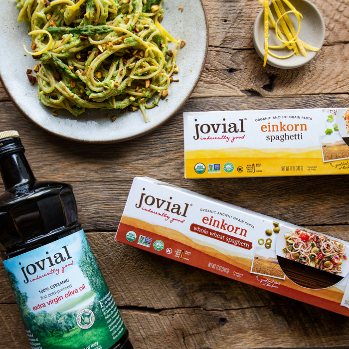 Creamy asparagus and ricotta spaghetti plated with Jovial Einkorn spaghetti boxes and a bottle of extra virgin olive oil on a wooden table