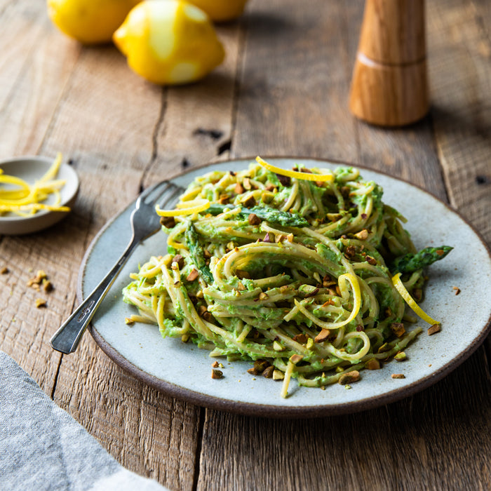 Einkorn spaghetti tossed in creamy asparagus-ricotta sauce with lemon zest and chopped pistachios on a ceramic plate