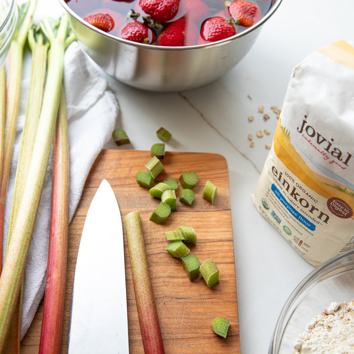 Chopped rhubarb on a cutting board with strawberries in a bowl and a bag of Jovial einkorn flour