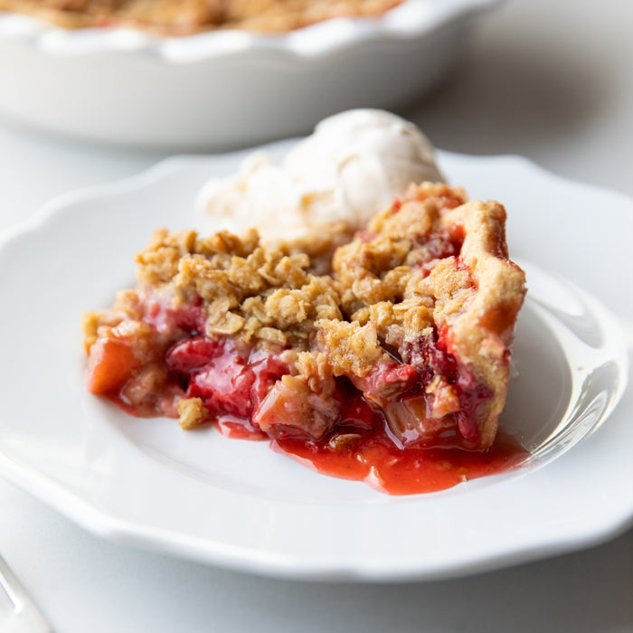 Slice of strawberry-rhubarb pie with einkorn crust and crumble topping, served with vanilla ice cream on white plate