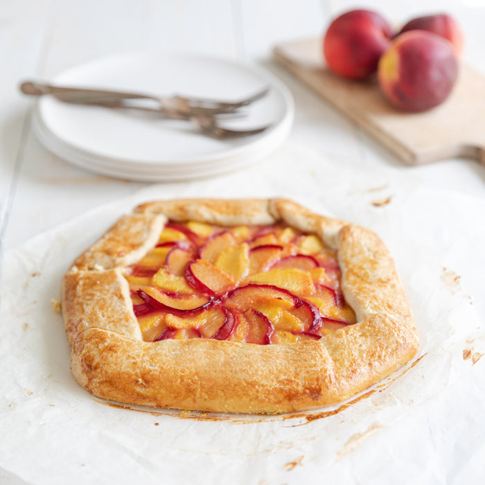 Three-quarter view of an Einkorn summer fruit galette showing golden flaky crust and sliced peaches and plums on parchment