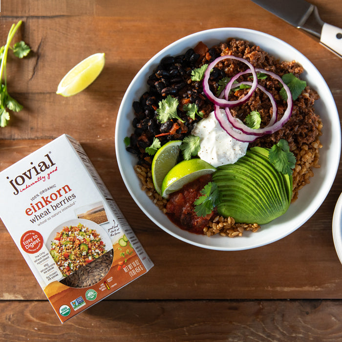 Overhead taco bowl of Einkorn wheat berries topped with avocado, black beans, seasoned beef and lime, with a Jovial Einkorn box on a wooden table