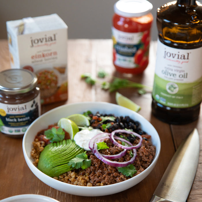Einkorn wheat berry taco bowl with beef, black beans, avocado, red onion, sour cream, and lime on wooden table