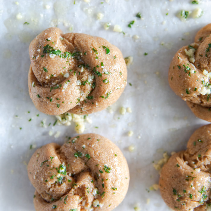 Overhead view of whole grain Einkorn garlic knots showing golden brown texture and garlic parsley topping on parchment paper