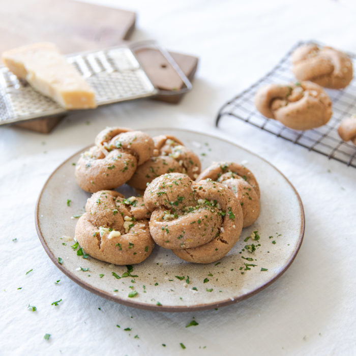Plate of whole-grain einkorn garlic knots garnished with minced garlic and parsley, grater and cooling rack in background
