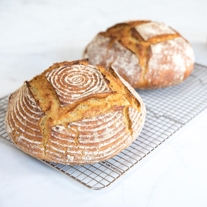 Three-quarter view of two Einkorn sourdough loaves with golden crust and banneton spiral pattern on cooling rack