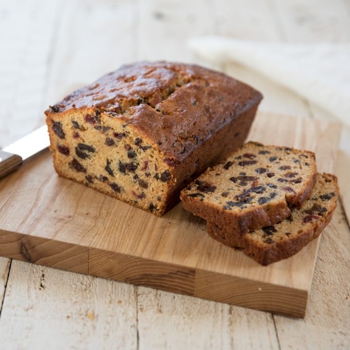 Sliced honey-sweetened rum fruit cake loaf showing dried fruit and raisins on a wooden cutting board