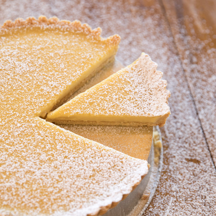 Overhead view of an Einkorn lemon cream tart with one slice removed, dusted with powdered sugar on a wooden surface