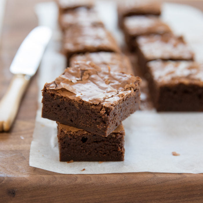 Close-up of two fudgy Einkorn mocha brownies stacked, showing glossy crackly top on a parchment-lined wooden board
