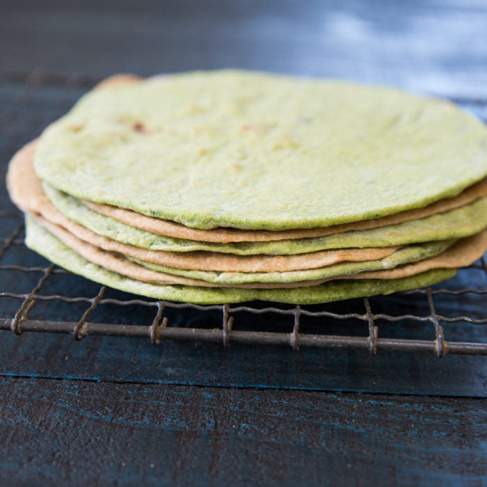 Side view of stacked Einkorn spinach tortillas showing thin rustic texture on a wire cooling rack over dark wood