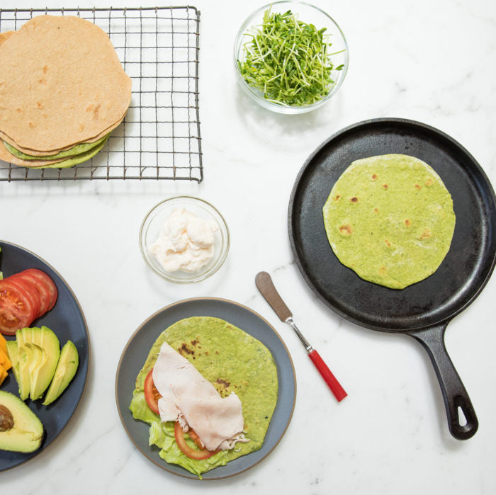 Overhead view of spinach and Einkorn tortillas, one on a skillet and one plated with avocado, tomato, turkey