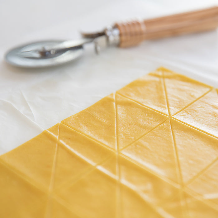 Dough sheet scored into diamond shaped pieces for olive oil chips with pastry cutter in soft focus background