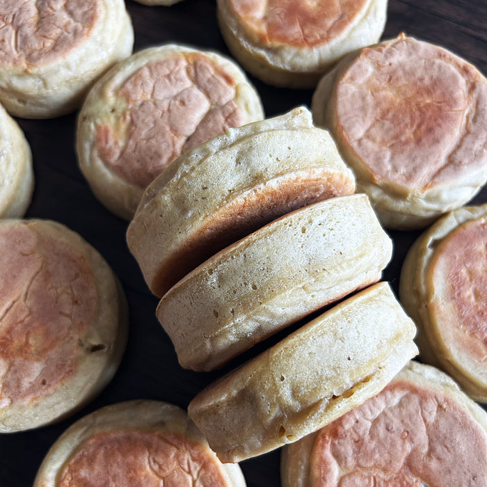 Overhead view of sourdough einkorn English muffins with golden toasted tops and airy interior on dark wood