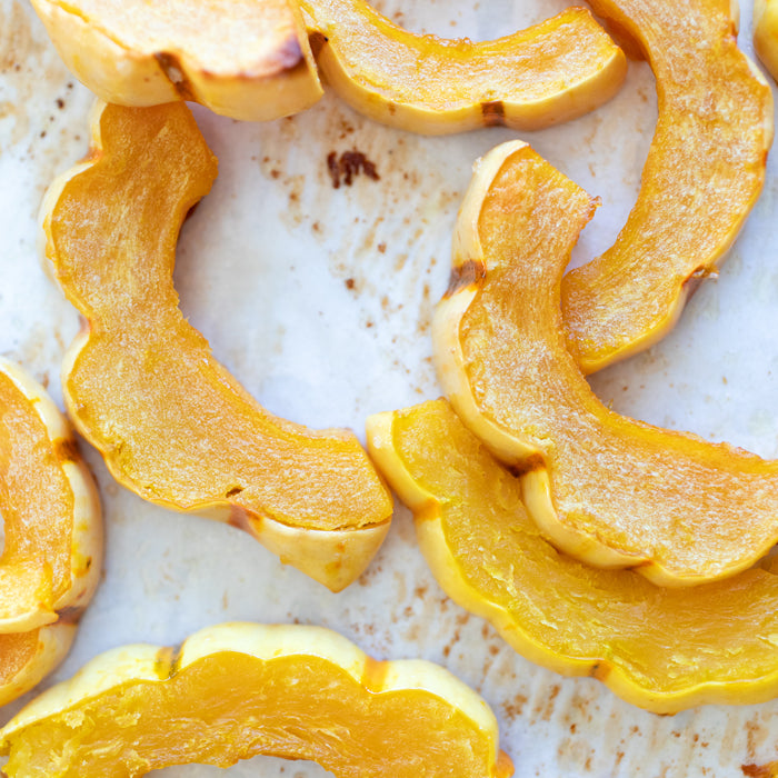 Close-up of roasted delicata squash slices showcasing caramelized golden flesh on a parchment-lined baking sheet