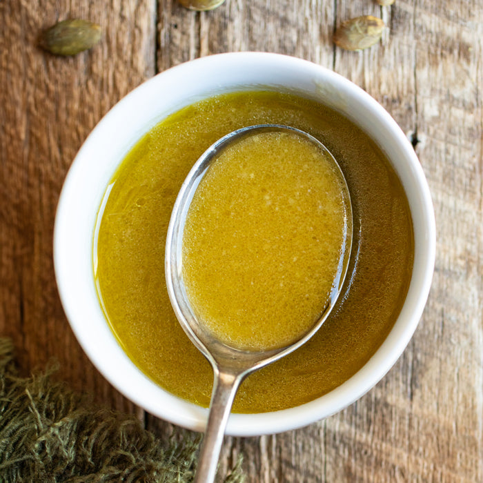 Top-down view of a white bowl of maple miso dressing with a spoon, smooth golden vinaigrette on a rustic wooden surface
