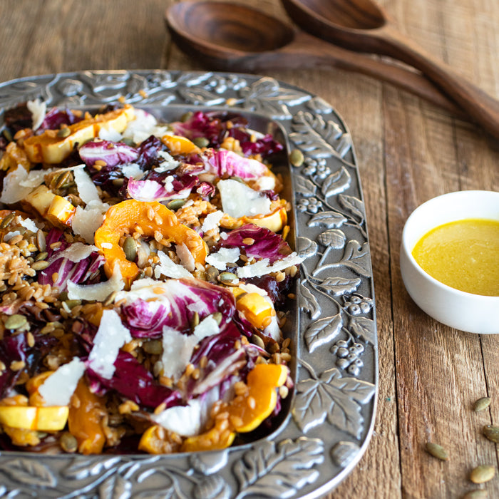 Wheat berry salad with roasted delicata squash, radicchio, and pepitas on a decorative metal tray with dressing beside it