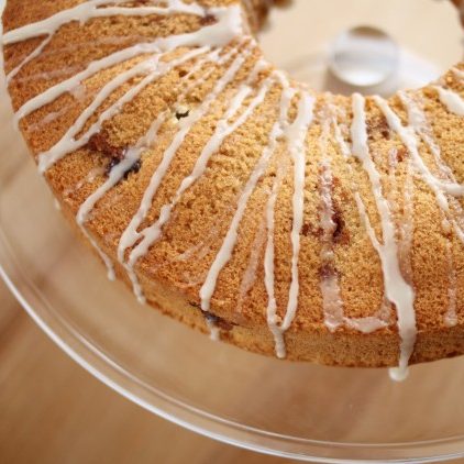 Top-down close-up of an olive oil bundt cake with thin white glaze on a glass cake stand