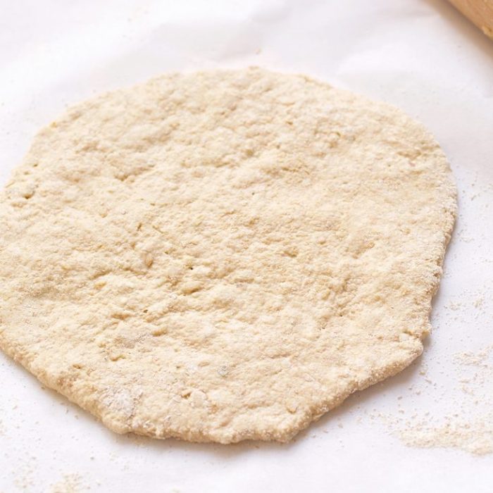Overhead view of a rolled whole grain einkorn flatbread dough dusted with flour on a white parchment-lined surface