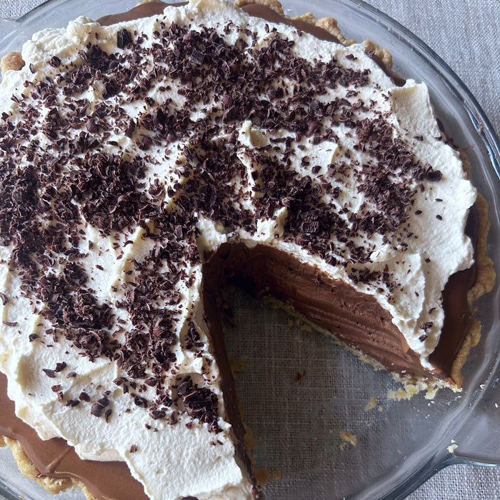 Top-down view of einkorn French silk pie with chocolate mousse, whipped cream and shaved chocolate, one slice removed