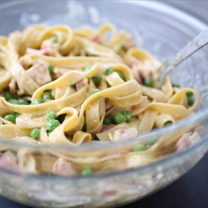 Close-up of tagliatelle carbonara gluten-free pasta bake with peas and bacon in creamy sauce in a glass bowl