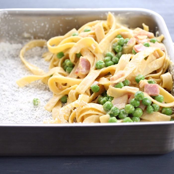 Close-up of gluten-free tagliatelle carbonara in a baking pan with peas, diced ham, and creamy sauce