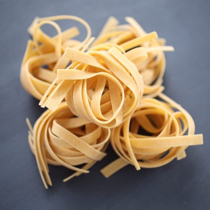 Top-down view of dry gluten-free tagliatelle nests showing ribbon-like strands on a dark slate background