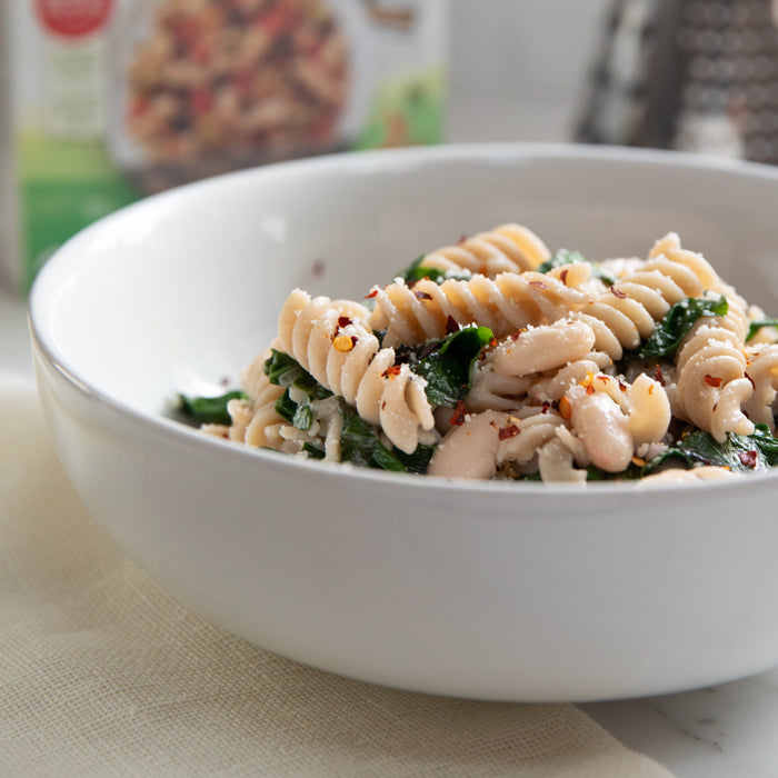 Bowl of gluten-free fusilli tossed with cannellini beans and wilted Swiss chard in a white bowl on a table