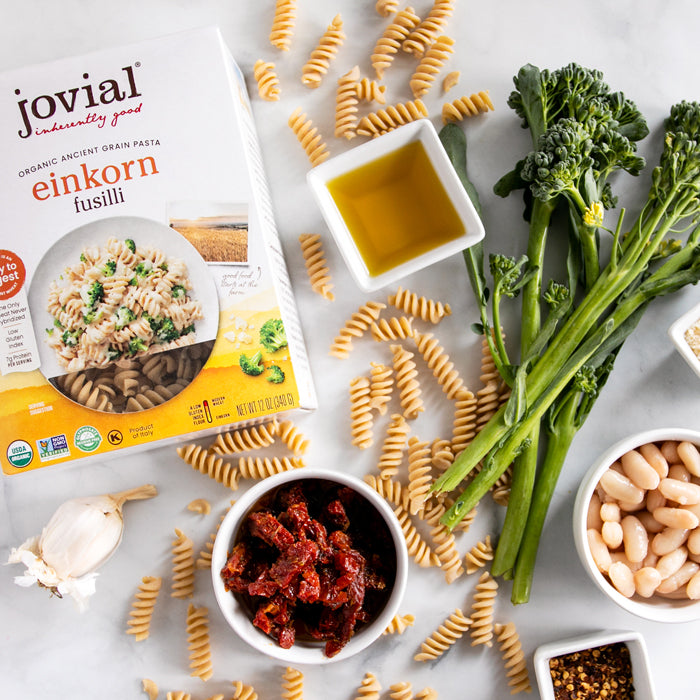 Einkorn fusilli pasta box with rapini, cannellini beans, sun-dried tomatoes, olive oil and garlic laid out for a recipe