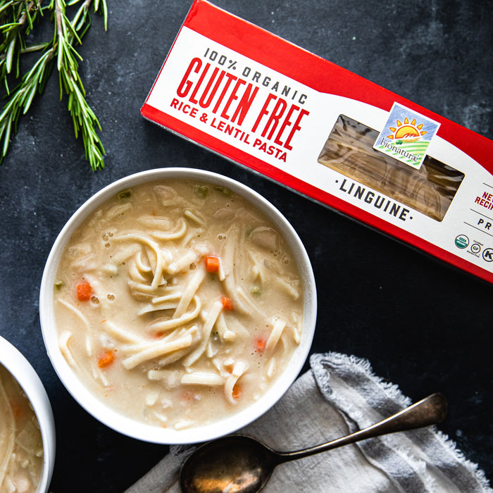 Bowl of creamy cannellini bean soup with broken linguine next to a box of gluten free linguine on a dark stone surface