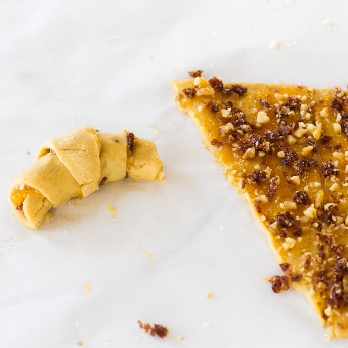 Rugelach made with einkorn dough: jam-and-nut filling spread on a triangular dough piece beside a rolled cookie on parchment