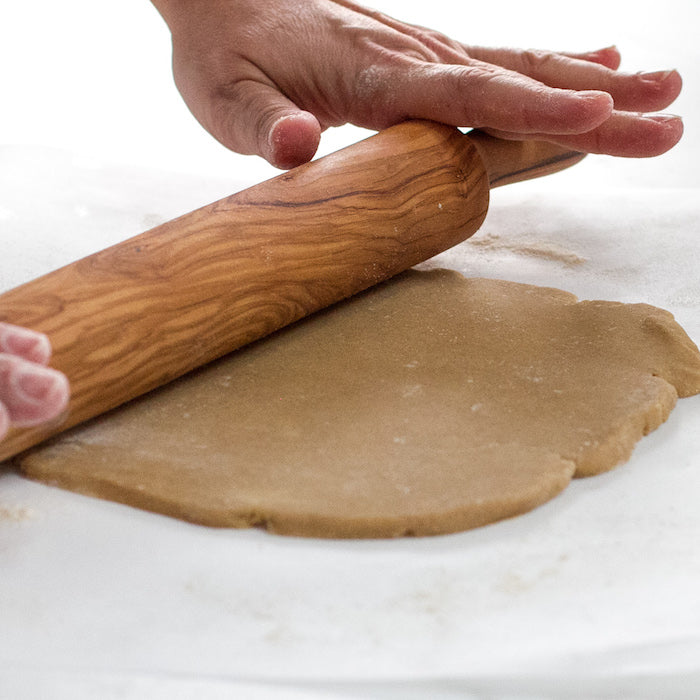 Hands rolling Einkorn sugar cookie dough with a wooden rolling pin on a lightly floured surface