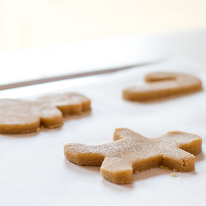 Close-up of Einkorn sugar cookie dough cut into holiday shapes on parchment paper, ready to bake