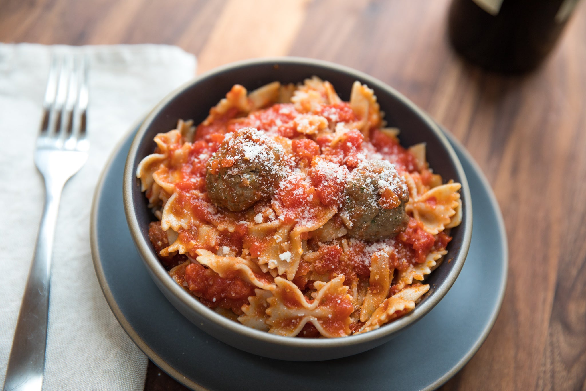 Cooked organic sourdough farfalle tossed in marinara sauce with meatballs on a blue plate on a wooden table