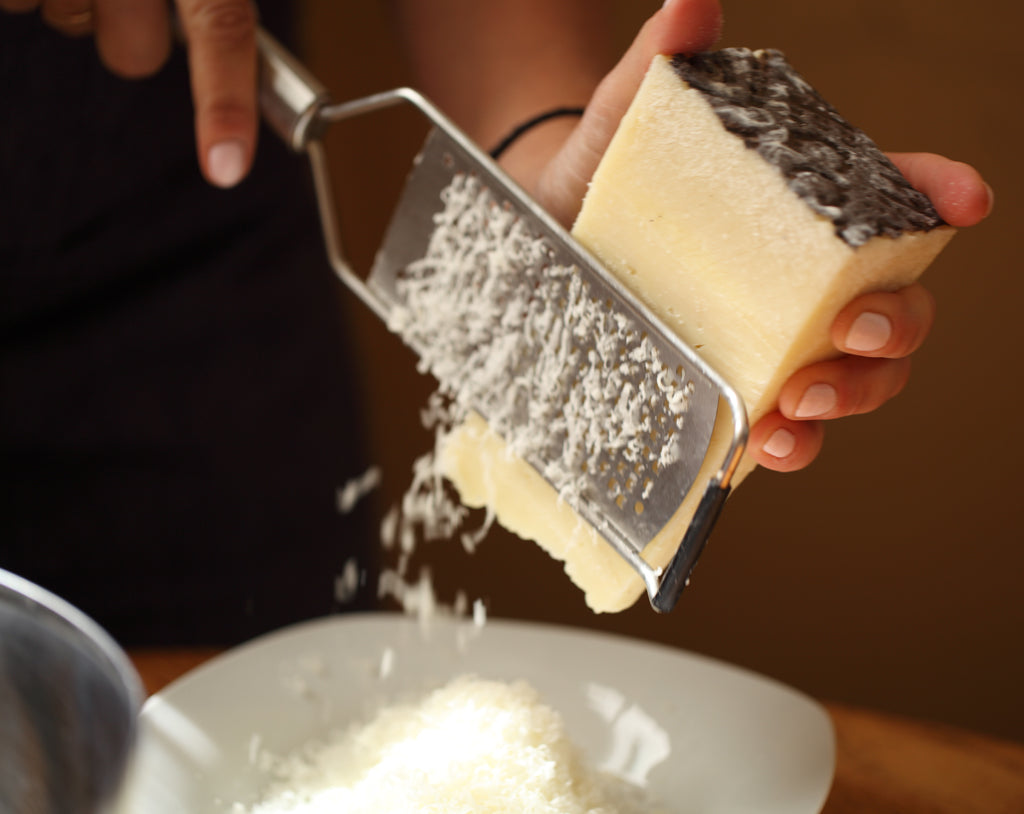 Hands grating hard Italian cheese with a handheld grater over a plate for gluten-free vegetarian lasagna