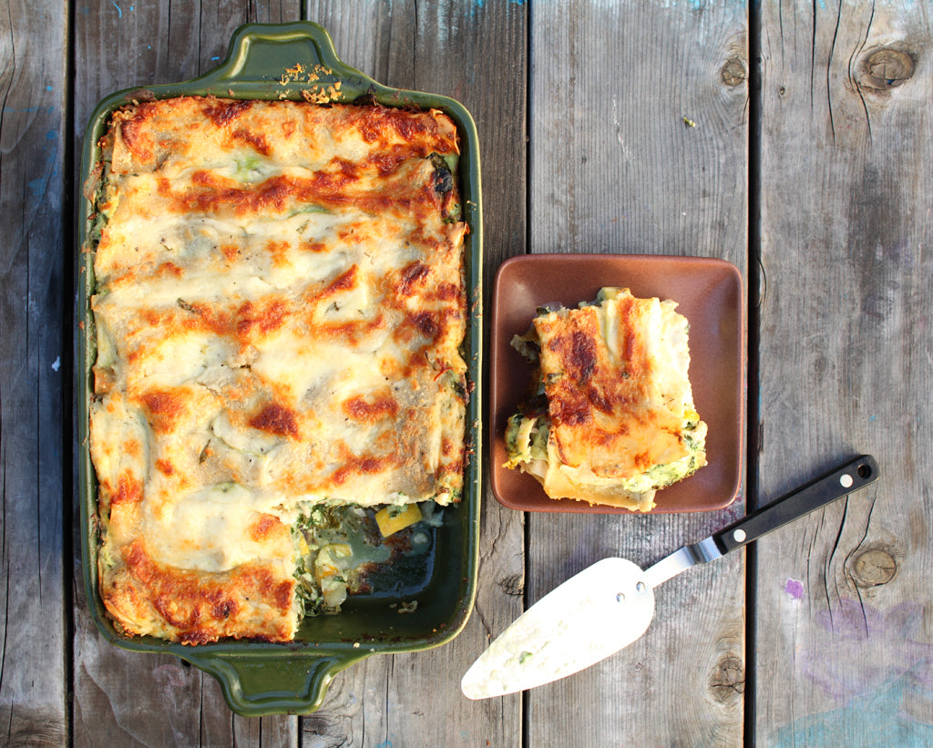 Gluten-free vegetarian lasagna baked golden, one slice on a small plate next to a green baking dish on a wooden table