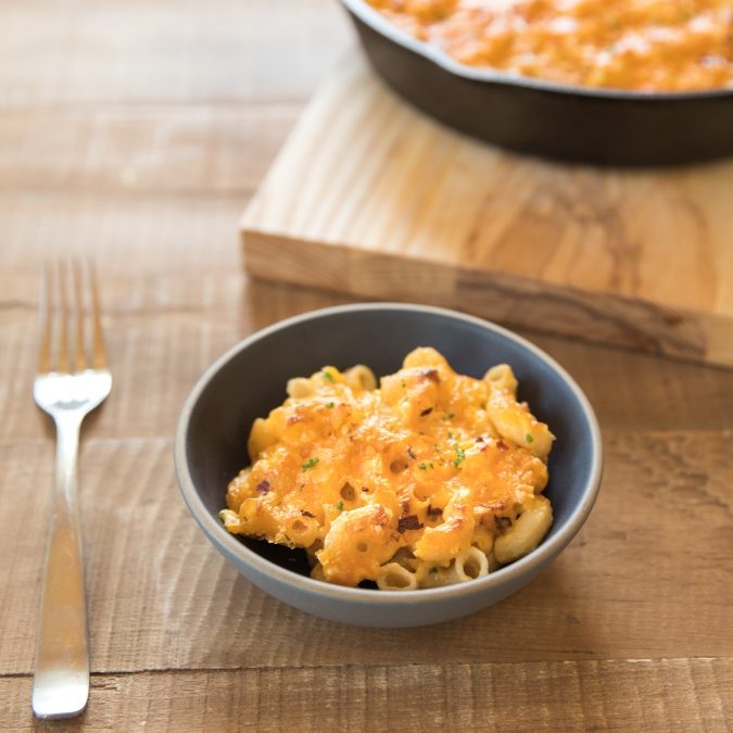 Bowl of skillet-baked gluten-free mac and cheese with melted golden cheddar, served on a wooden table with the skillet in the background