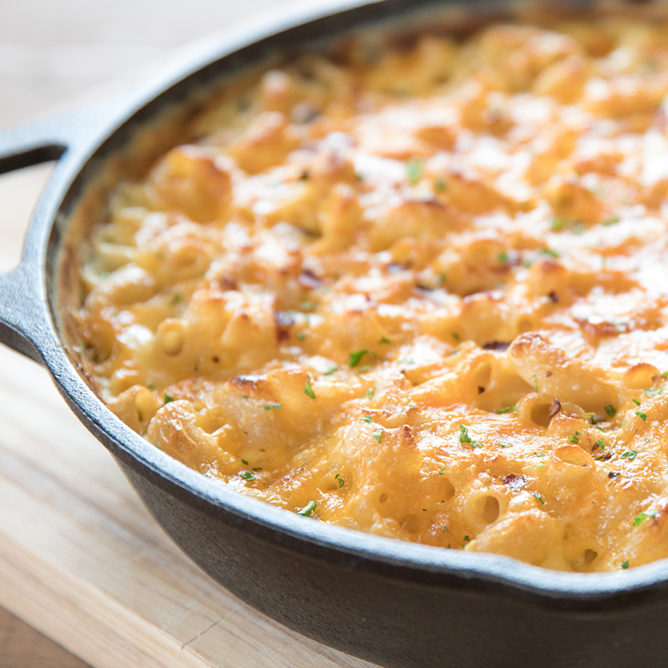 Baked macaroni and cheese in a cast-iron skillet with melted, lightly browned cheddar and a sprinkle of parsley