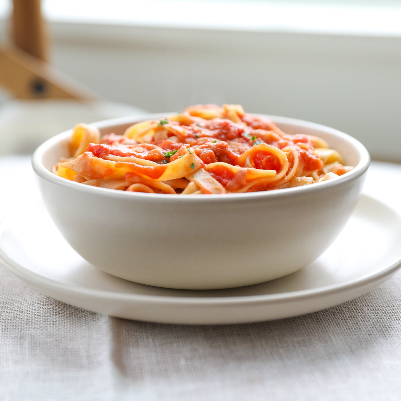 Gluten-free tagliatelle dressed in tomato sauce served in a white bowl on a linen-covered table