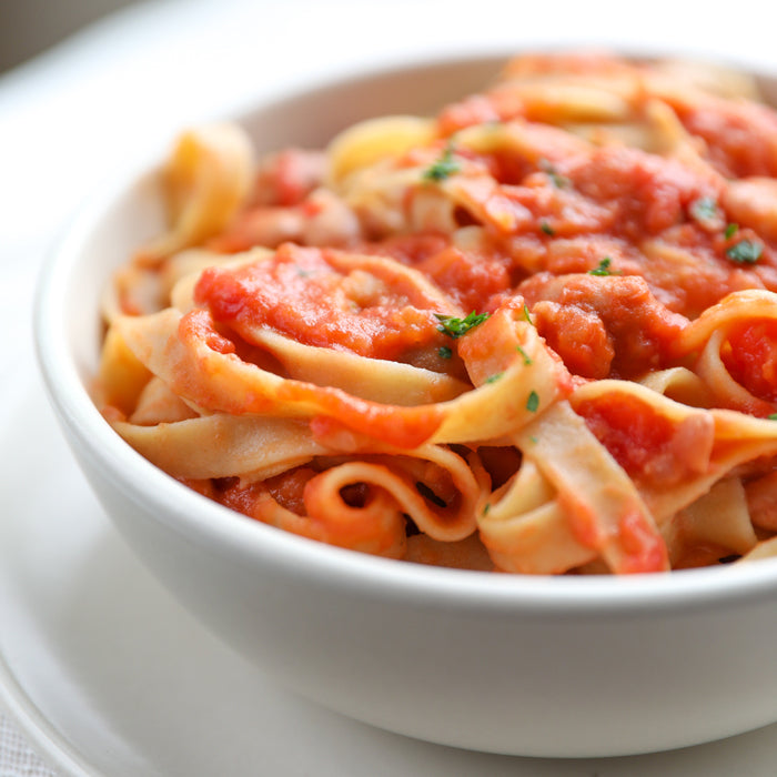 Close-up of gluten-free tagliatelle in a white bowl showcasing ribbon-shaped pasta coated in chunky borlotti bean tomato sauce