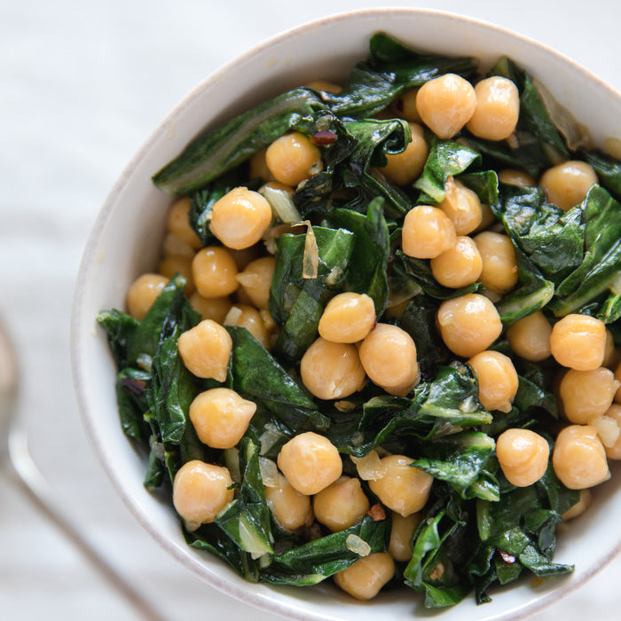 Bowl of garlic-sautéed chickpeas and wilted greens in a white bowl on a light cloth background