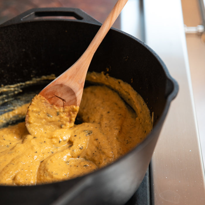 Butternut squash pasta sauce being stirred with a wooden spoon in a cast-iron pot on a stovetop