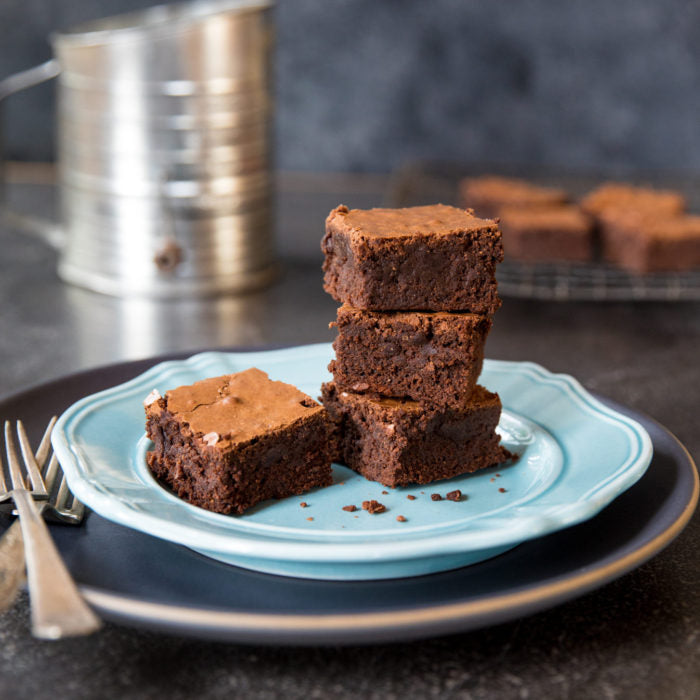 Close-up of stacked mocha fudge brownies made with einkorn, showing fudgy interior on a blue plate with sifter behind
