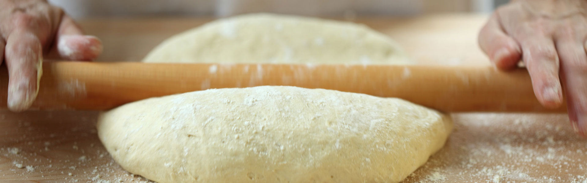 Hands rolling dough with a wooden rolling pin on a floured wooden board.