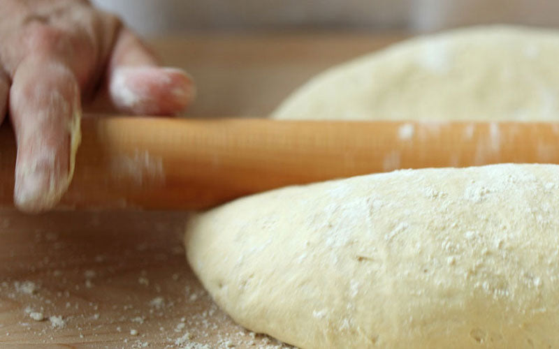 Hands rolling dough with a wooden rolling pin on a floured surface