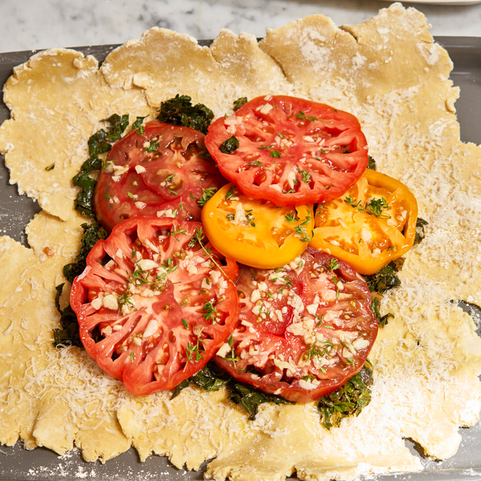 Overhead view of unbaked Einkorn BLT galette with heirloom tomato slices and kale on a floured baking sheet