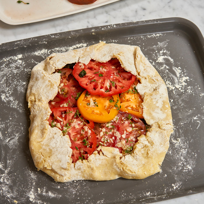 Einkorn BLT galette with flaky crust topped with red and yellow heirloom tomato slices and chopped herbs
