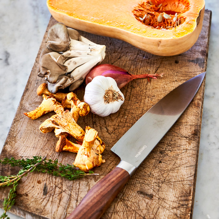 Halved butternut squash, chanterelle and oyster mushrooms, garlic, shallot, thyme, and knife on a wooden cutting board