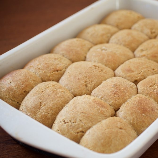 Close-up of 20 whole-grain einkorn dinner rolls in a white baking dish showcasing golden-brown crusts on a wooden table